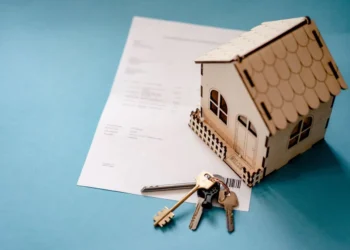 Wooden replica house and a set of keys sit on a blue desktop. A Home Equity Loan can be used beneficially in multiple ways.