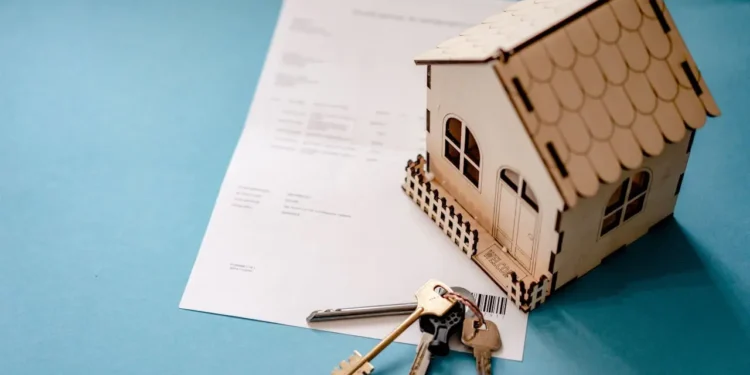 Wooden replica house and a set of keys sit on a blue desktop. A Home Equity Loan can be used beneficially in multiple ways.