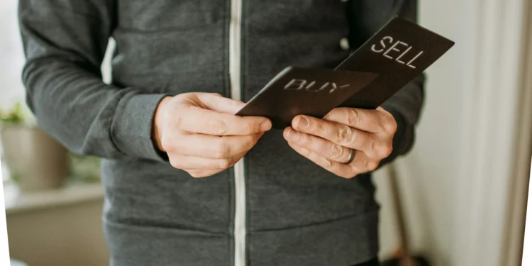 A man holds two cards that say Buy and Sell. Index funds vs ETFs - which one is better for your investing strategy?