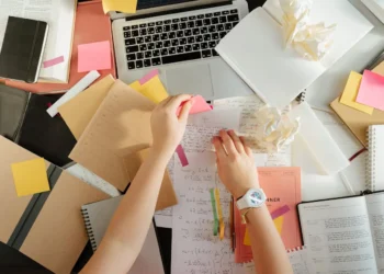 Two hands move paper around a messy desk. Avoid these beginner investment mistakes by cleaning up your best practices.