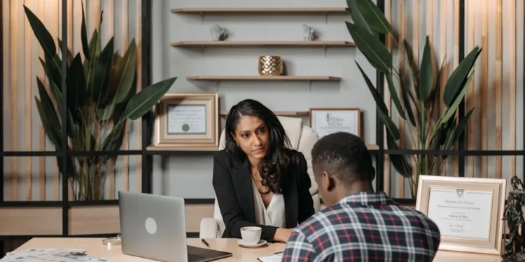 A man and woman sit across a desk from each other, looking at paperwork. Our estate planning guide can help your process.