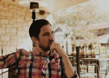 A man in a plaid shirt sits at a table, looking off in the distance. Being aware of anchoring bias will help you become a better investor