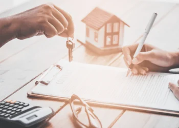 A hand dangles keys above a desk. Your mortgage principal & interest is part of your monthly payments.