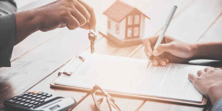 A hand dangles keys above a desk. Your mortgage principal & interest is part of your monthly payments.