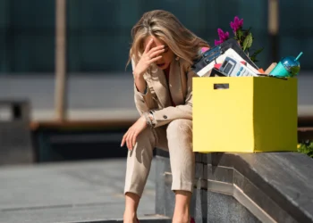 Woman sits on cement bench with box of office supplies. Being laid off is not the end.