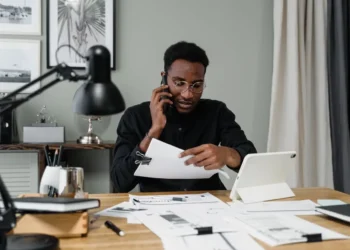 Man in black long sleeved shirt sits at a desk looking at papers. To stick to a budget can be hard, but you can actually do it!