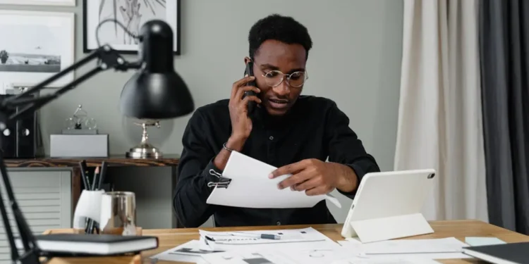 Man in black long sleeved shirt sits at a desk looking at papers. To stick to a budget can be hard, but you can actually do it!