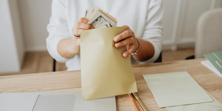 A woman folds a stack of dollar bills into an envelope from her money hacks.