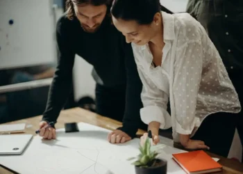 Two people stand over a desk, looking at a large paper. Personal development is key for career development.