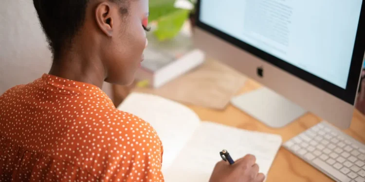 Woman sits at desk and writes in notebook. Follow these freelancer tips.