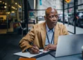 Man takes notes while reading financial literacy resources on a laptop.