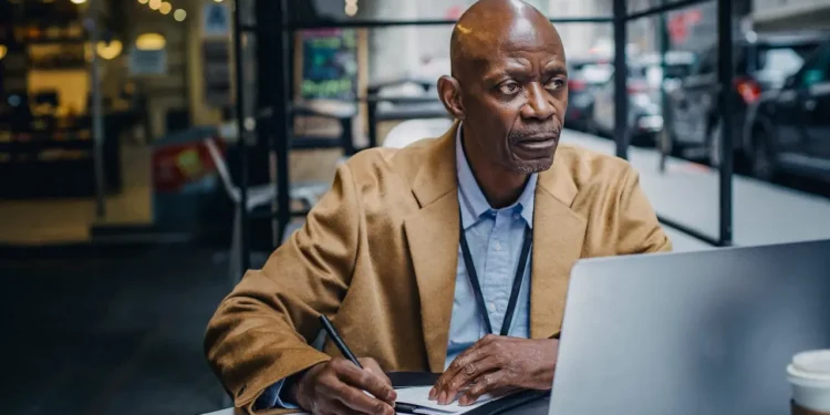 Man takes notes while reading financial literacy resources on a laptop.