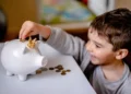 Little boy happily puts coins into a white piggy bank.