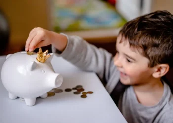 Little boy happily puts coins into a white piggy bank.