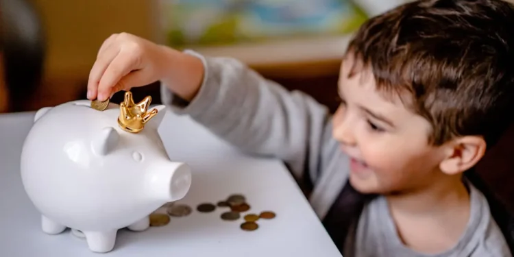 Little boy happily puts coins into a white piggy bank.