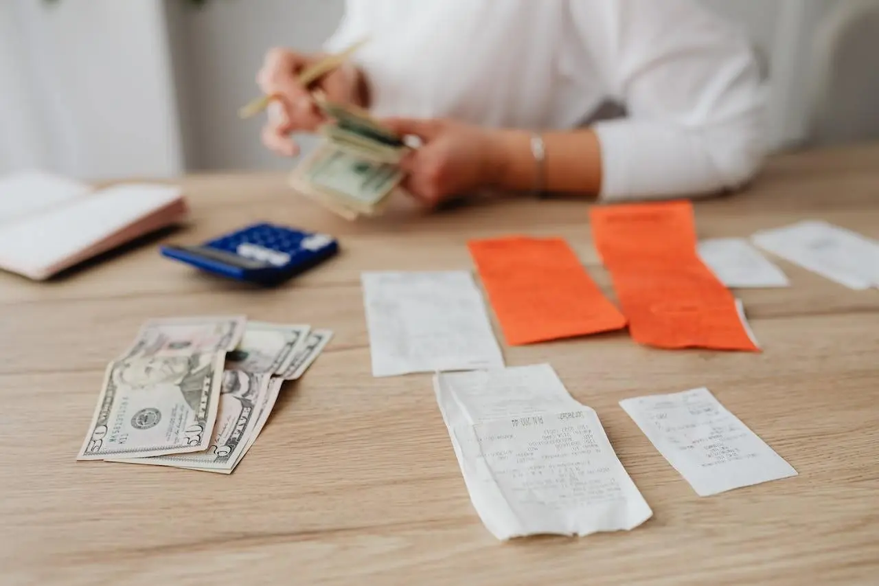 Receipts and bills on a desk, someone counting money. Having weekly financial check-ins can help you reach your goals faster.