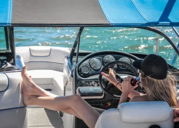 Woman in black cap lounges at the wheel of a boat. Lifestyle creep sneaks up on you.