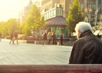 A senior man sits on a sunny bench in a town square. Does old school retirement advice still apply?