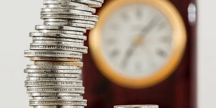 a stack of coins in front of a clock - compound interest adds up over time.