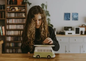 Little girl putting money in a piggy bank - financial literacy for kids is so important to teach.