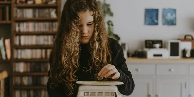 Little girl putting money in a piggy bank - financial literacy for kids is so important to teach.