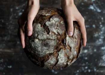 Two hands hold a dark loaf of bread. make at home food can save you a bundle.