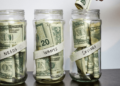 Three glass jars full of money with the labels Needs, Wants and Savings. How to set up the 50/30/20 budget ratio.