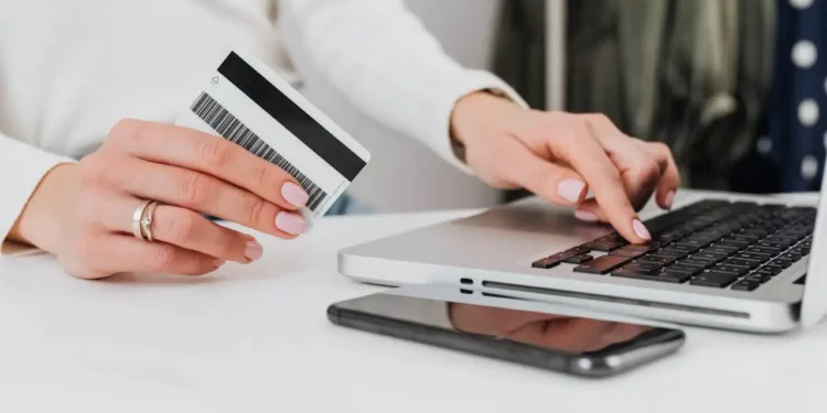 Someone holds a credit cards while typing on a laptop. Your credit utilization ratio tells lenders how likely you are to pay back debt.