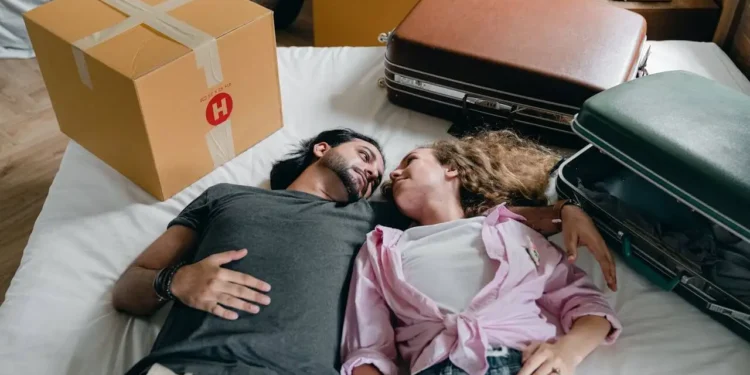 Two people lay on a bed surrounded by moving boxes - if you pay off your mortgage faster it will be a relief!