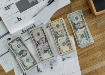 four stacks of dollar bills on top of paperwork and household debt bills.