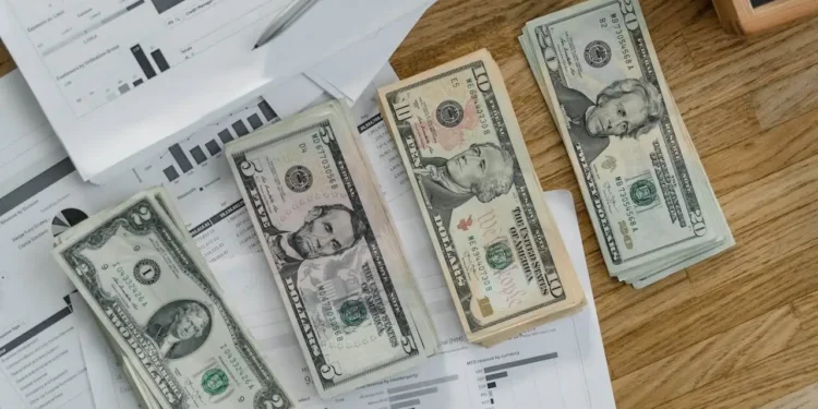 four stacks of dollar bills on top of paperwork and household debt bills.