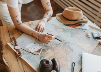 A person leans on a desk that is covered in a map. This two month travel planning guide will help you plan your ultimate trip!
