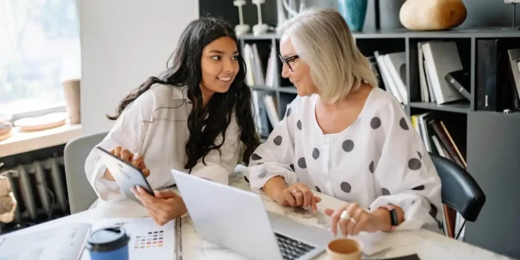 A young woman and older woman look at a tablet at a desk in a bright office. We wish someone had told us how retirement works!