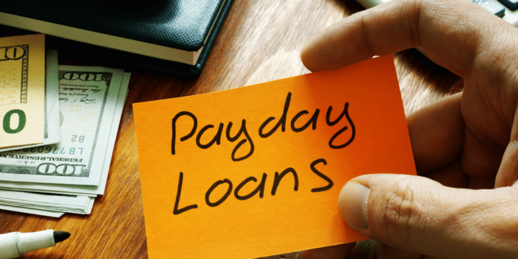 A hand holds an orange post-it that says Payday Loans on it.