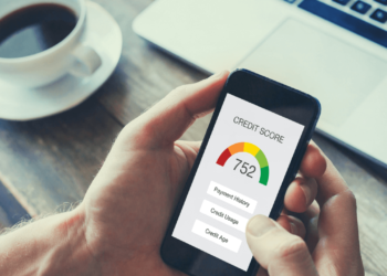 Someone holds their phone in their hand above their desk. These questions can help you raise your credit score.