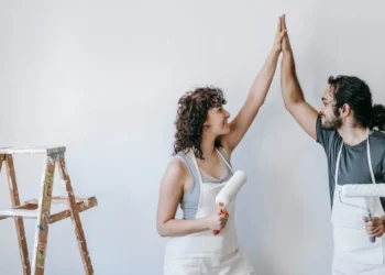A man and woman high five while holding paint rollers. Home equity improvements can be as simple as refreshing your wall paint.