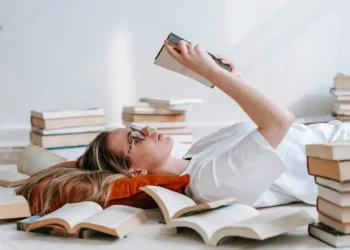 A woman lays on her back reading, surrounded by books. Financial literacy can be learned by anyone!