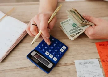A hand works on a calculator while the other hand holds a stack of cash. If you're struggling with your finances, take these seven steps.