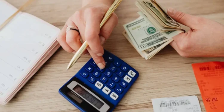 A hand works on a calculator while the other hand holds a stack of cash. If you're struggling with your finances, take these seven steps.