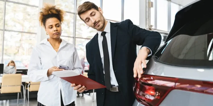 A woman stands in a car dealership, listening to a salesperson.