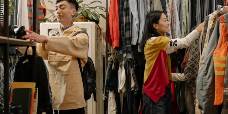 A man and woman search through racks while thrifting in a store.