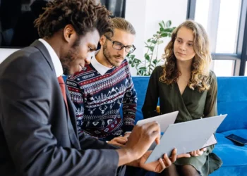 A man in a suit sits with two people, all looking at something on a screen. If you cosign on a loan, you are responsible to pay it off.