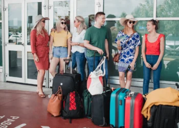 A group of people wait outside an airport with their baggage in front of them. If you want to save at the airport, get in the right mindset.