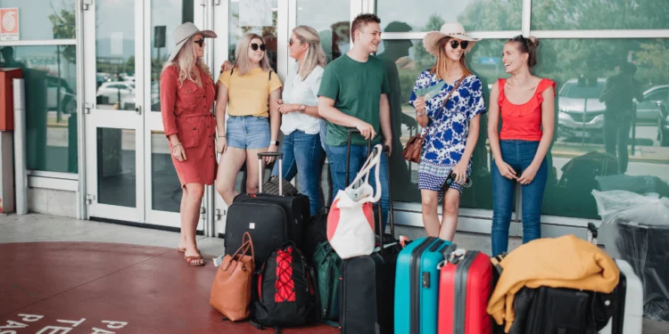 A group of people wait outside an airport with their baggage in front of them. If you want to save at the airport, get in the right mindset.