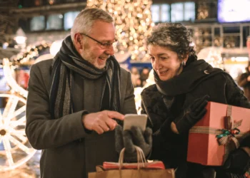 Two seniors look at their phone while holiday shopping. You can avoid going broke this holiday season with some financial discipline.