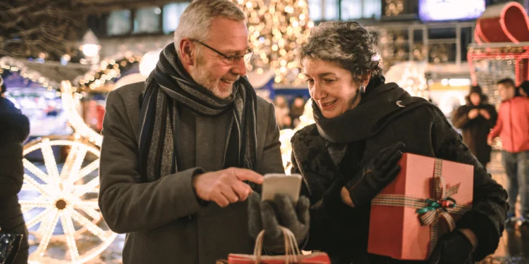 Two seniors look at their phone while holiday shopping. You can avoid going broke this holiday season with some financial discipline.