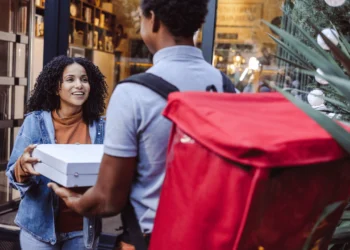 A woman takes pizza boxes from a delivery person. Convenience culture means we are just paying more for the things we could be doing ourselves.