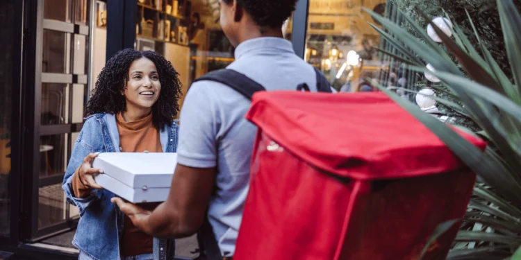 A woman takes pizza boxes from a delivery person. Convenience culture means we are just paying more for the things we could be doing ourselves.
