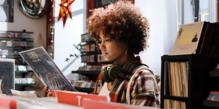 A woman wearing headphones looks at vinyl in a store. Making frugal mindset shifts will change your entire outlook.