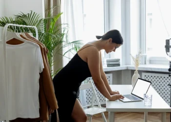 A woman stands over a desk working on a laptop in a small office. If you're self-employed, you should still be saving for your retirement.
